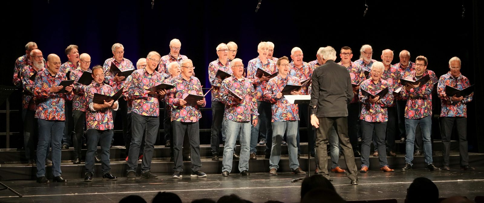 Der Liederkranz Kornwestheim auf der Bühne in bunten Hemden, singend, davor der Chorleiter.